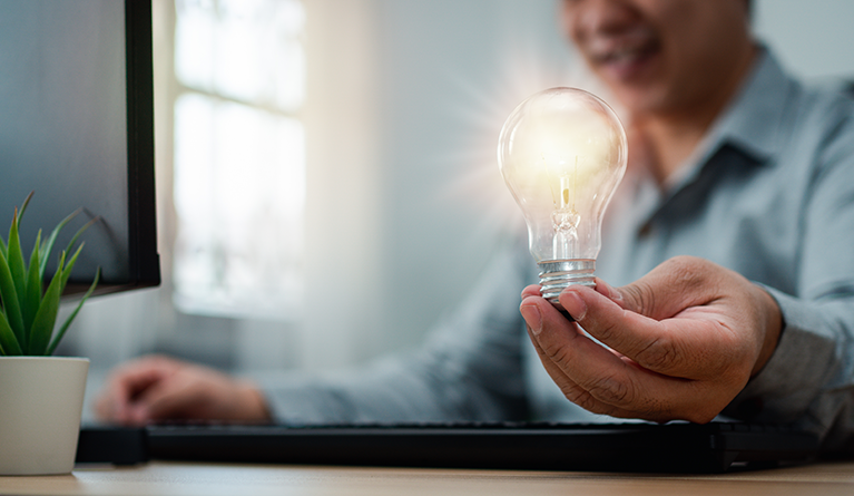 Picture-of-man-at-desk-holding-lit-up-bulb